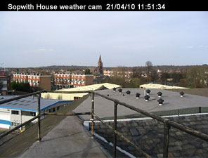Sopwith house weather cam. Taken on the 21/04/10 at 11:51 and 34 seconds.
In the foreground are the safety rails on the flat part of the roof. Nearby ther are low rise industrial buildings, beyond those are block of flats.
In the distance there's a church steeple.